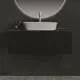 Waschtisch mit schwarzem Unterbau und runder, beleuchteter Spiegelwand. Ideal Standard Waschbecken in ovaler Form, kombiniert mit einem modernen Wasserhahn.